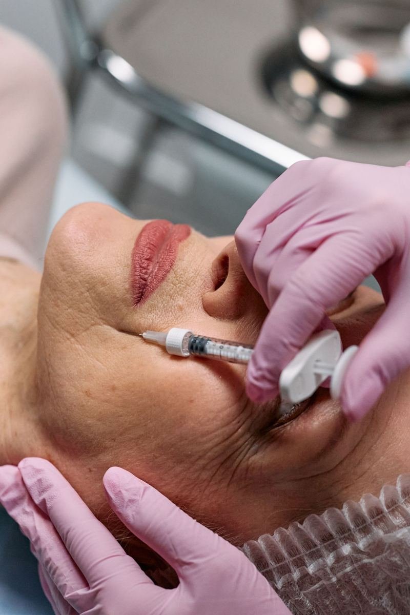 Profissional de luvas realizando procedimento estético injetável no rosto